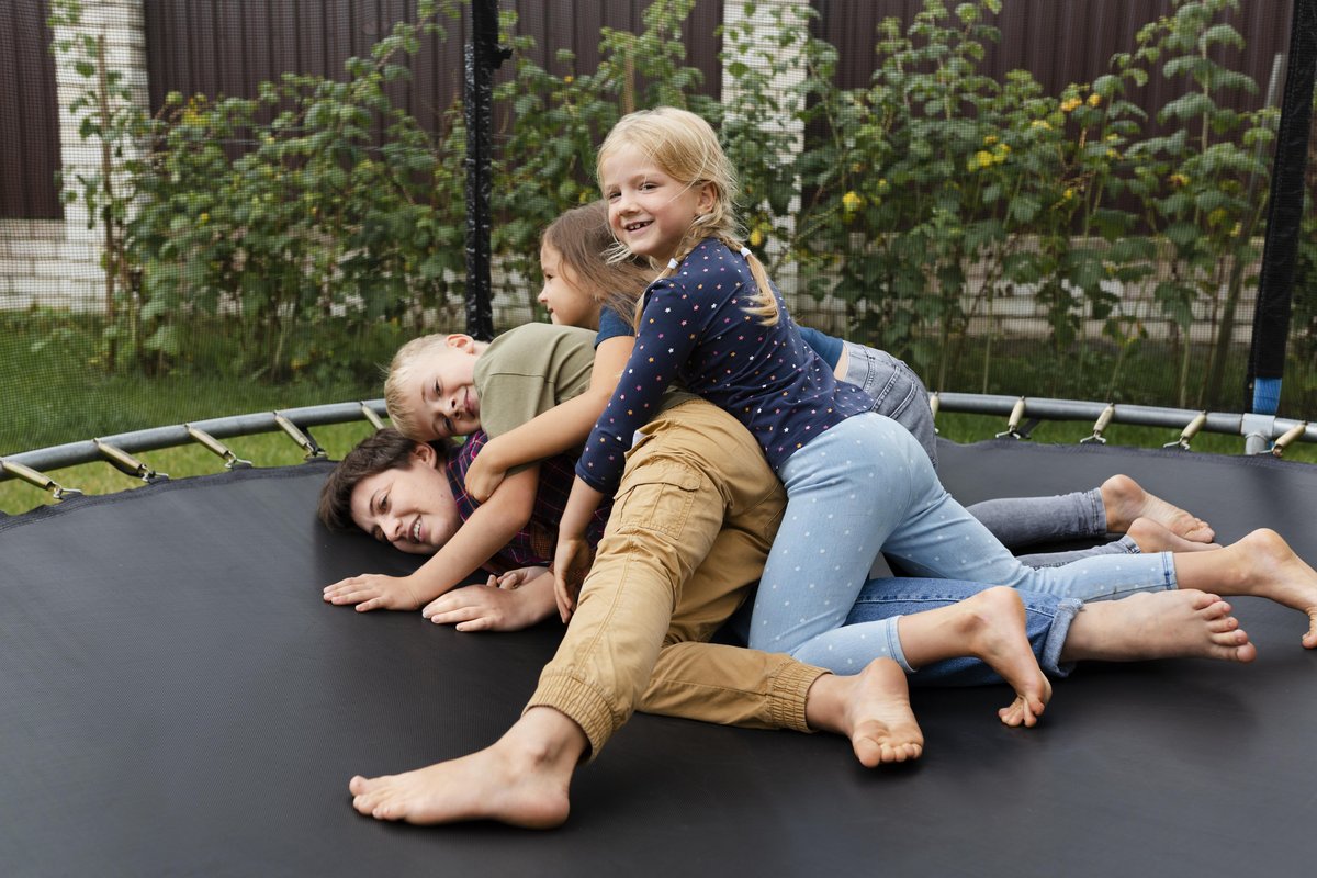 Maminka s dětmi dovádí na zahradní trampolíně