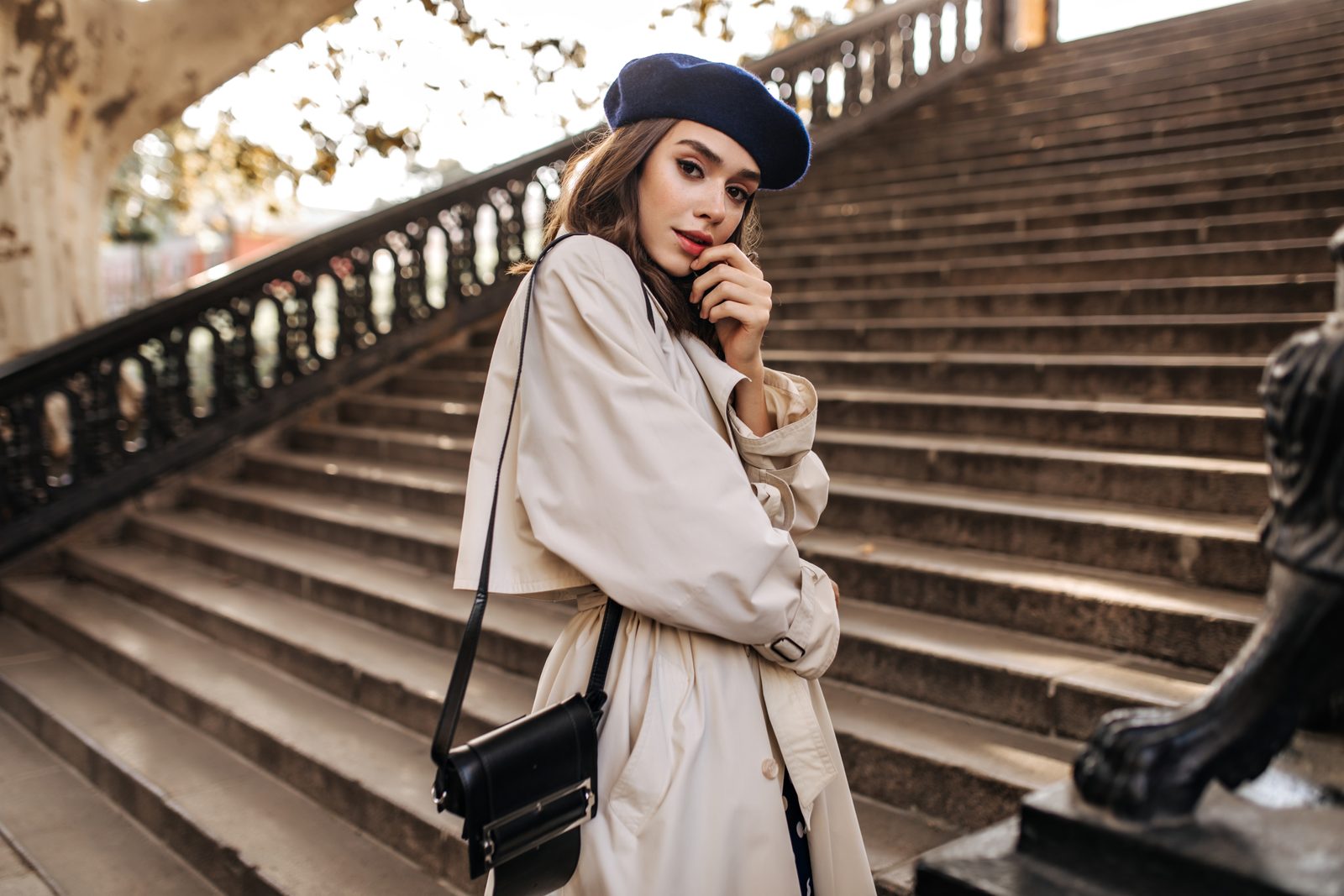 Žena v béžovém trenčkotu s baretem a crossbody kabelkou